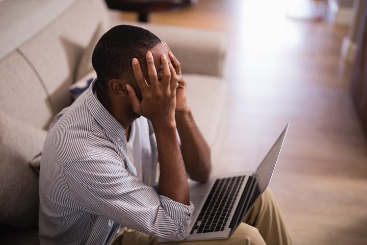 Black man sitting down and covering his face with a laptop in his lap - sex addiction