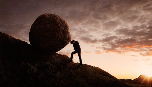 person pushing a boulder up a hill