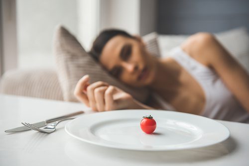 woman looking at plate with one small tomato on it