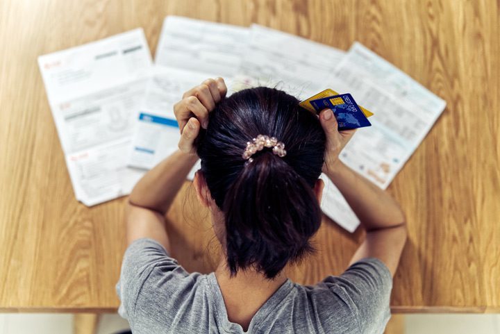 stressed woman holding credit cards and looking down at statements - compulsive shopping