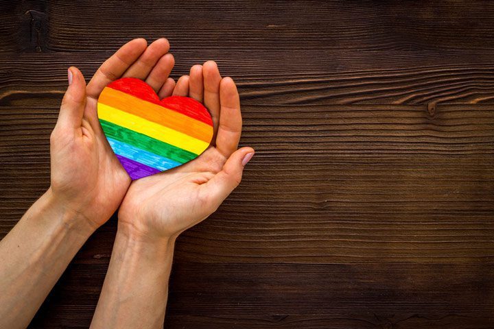 hands holding rainbow heart on dark wood background - LGBTQ(IA+)