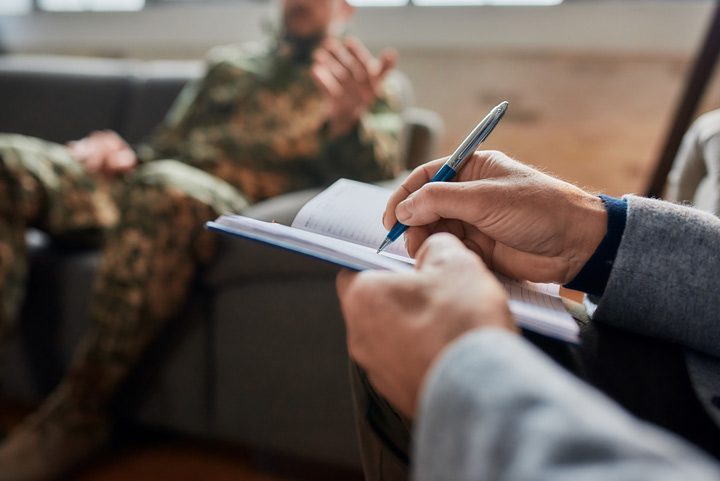 cropped shot of man in military fatigues talking to a therapist who is taking notes - treatment for veterans